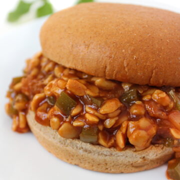 Vegan BBQ Tempeh Sloppy Joes in a wheat bun on a white plate