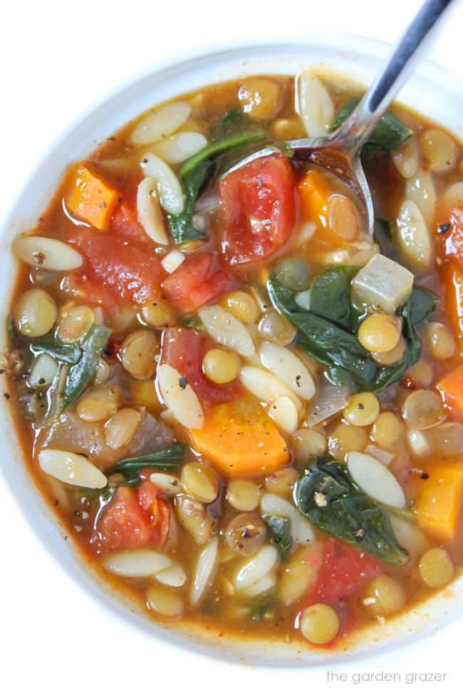 Vegan lentil orzo spinach soup in a bowl with spoon