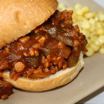 Vegan tempeh sloppy joes on a hamburger bun with a side of corn