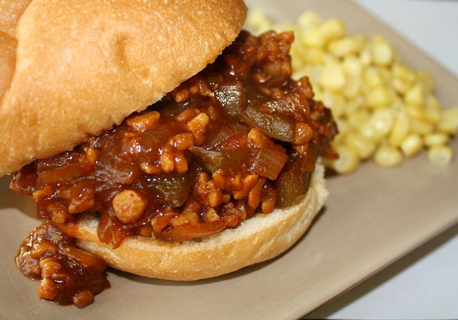 Vegan tempeh sloppy joes on a hamburger bun with a side of corn