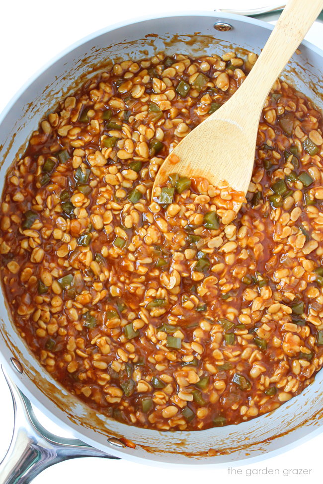 Vegan BBQ sloppy joe mixture cooking in a large skillet with wooden spoon