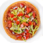 Vegan bean tostada on a white plate with romaine lettuce, onion, and tomato