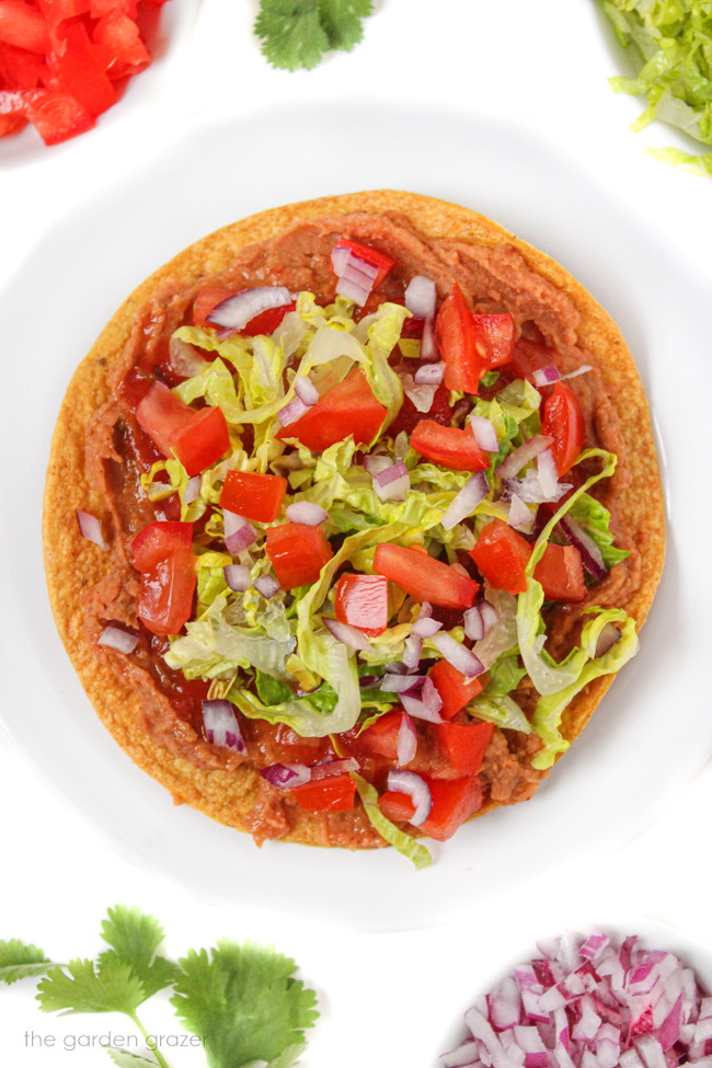 Vegan bean tostada on a white plate with romaine lettuce, onion, and tomato