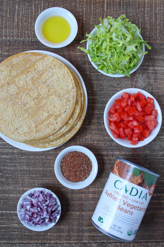 Corn tortillas, tomatoes, lettuce, onion, and refried beans ingredients on a wooden table