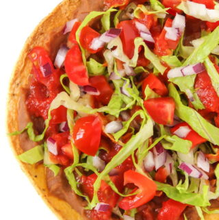Vegan tostada with refried beans, tomato, lettuce, and onion