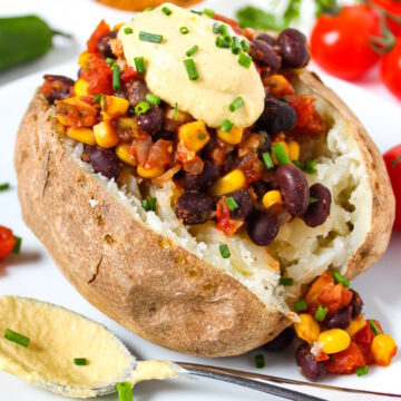 Mexican Fiesta Baked Potato on a white plate topped with cashew queso and chives