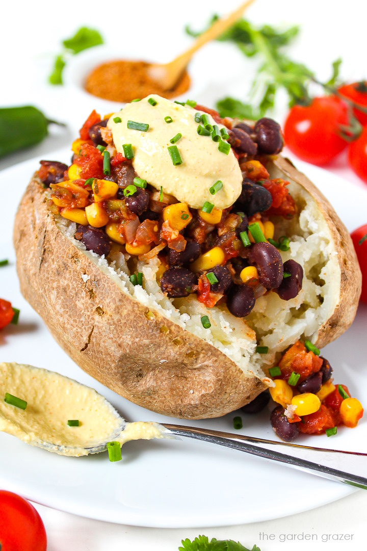 Mexican Fiesta Baked Potato on a white plate topped with cashew queso and chives