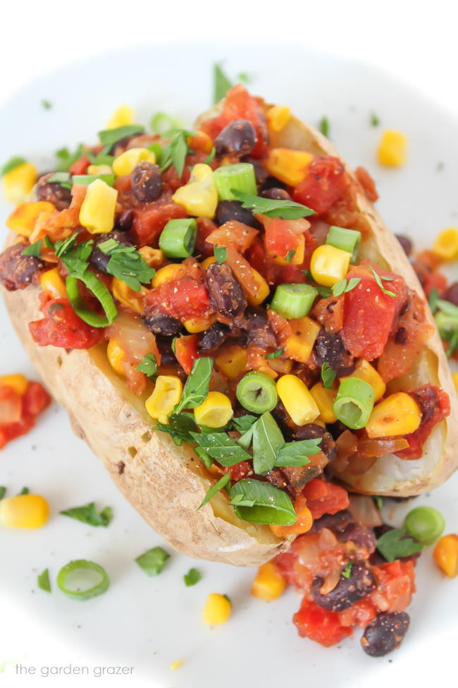 Potato on a plate with black beans, tomato, corn, and green onions