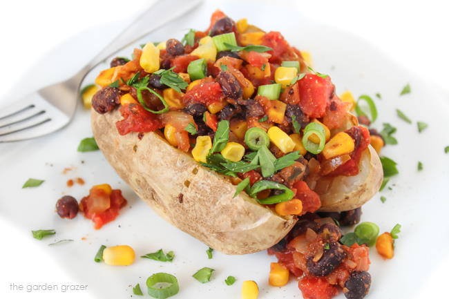 Baked potato on a plate stuffed with black beans, corn, and tomato