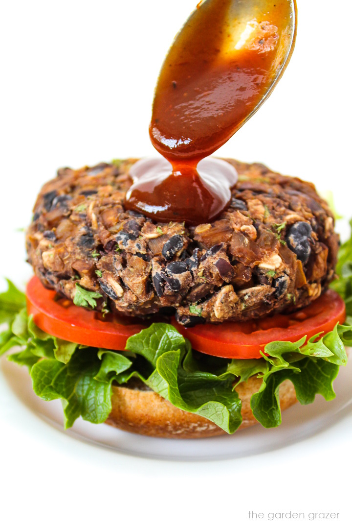 BBQ sauce being spooned on top of an open-faced black bean mushroom burger