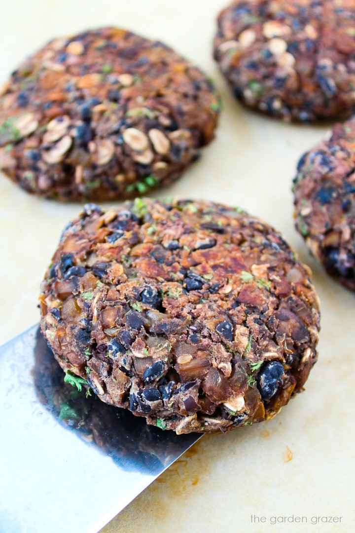 Metal spatula lifting up a black bean mushroom burger from a baking sheet