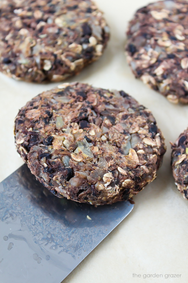 Vegan black bean burgers cooking on a sheet pan with spatula