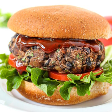 Side view of a black bean mushroom burger on a bun with lettuce, tomato, and BBQ sauce