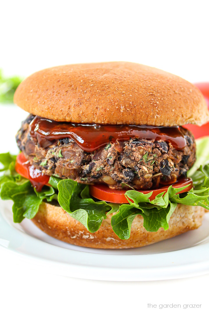 Side view of a black bean mushroom burger on a bun with lettuce, tomato, and BBQ sauce