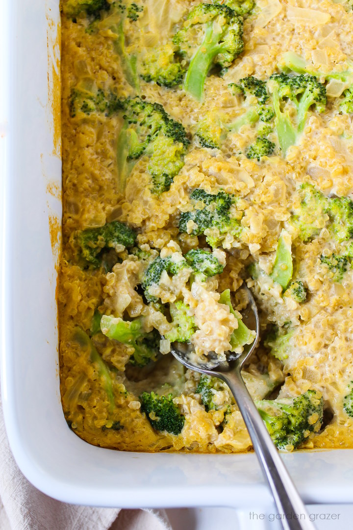 Overhead view of baked broccoli quinoa casserole in a white baking dish with serving spoon