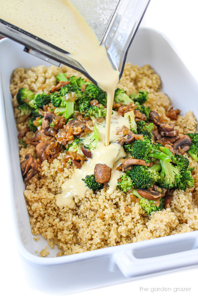 Pouring vegan cheese sauce from a blender into a prepared casserole dish