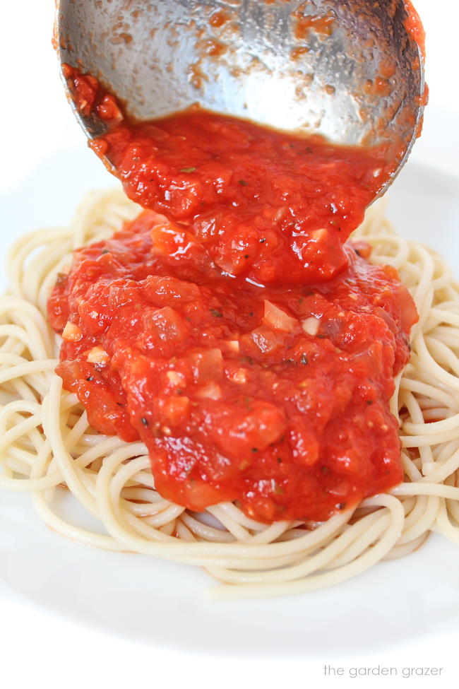 Oil free marinara sauce being poured over spaghetti pasta on a plate