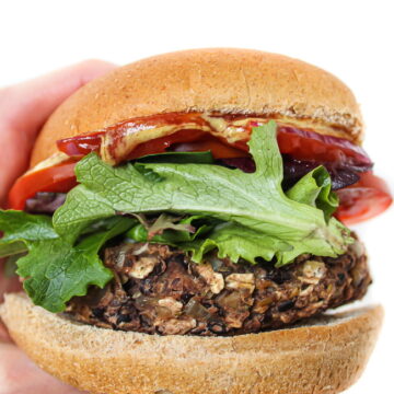Hand holding a vegan black bean mushroom burger in bun with toppings