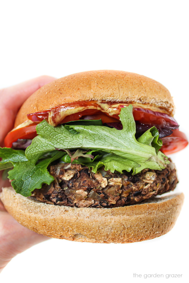 Hand holding a vegan black bean mushroom burger in bun with toppings
