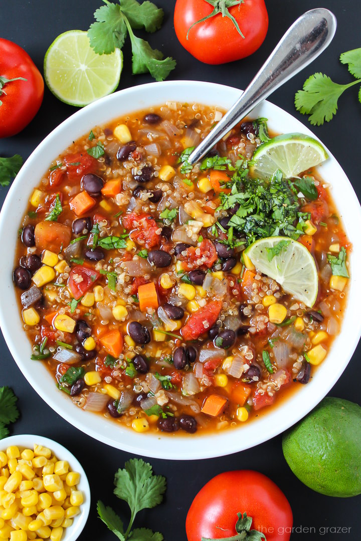 Vegan quinoa black bean soup in a white bowl garnished with lime slices and fresh cilantro