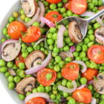 Bowl of roasted peas with mushrooms and tomato with a spoon
