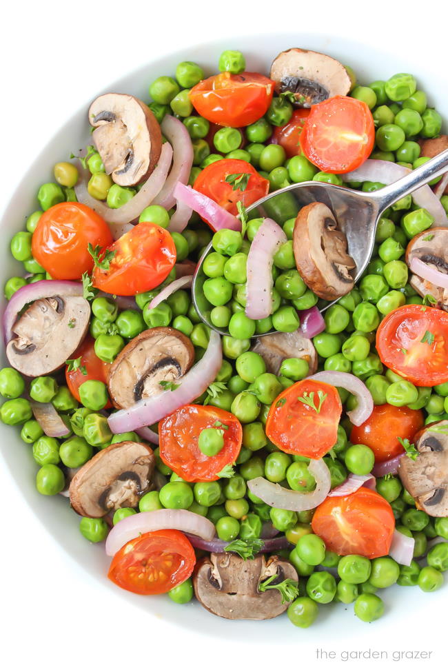 Bowl of roasted peas with mushrooms and tomato with a spoon