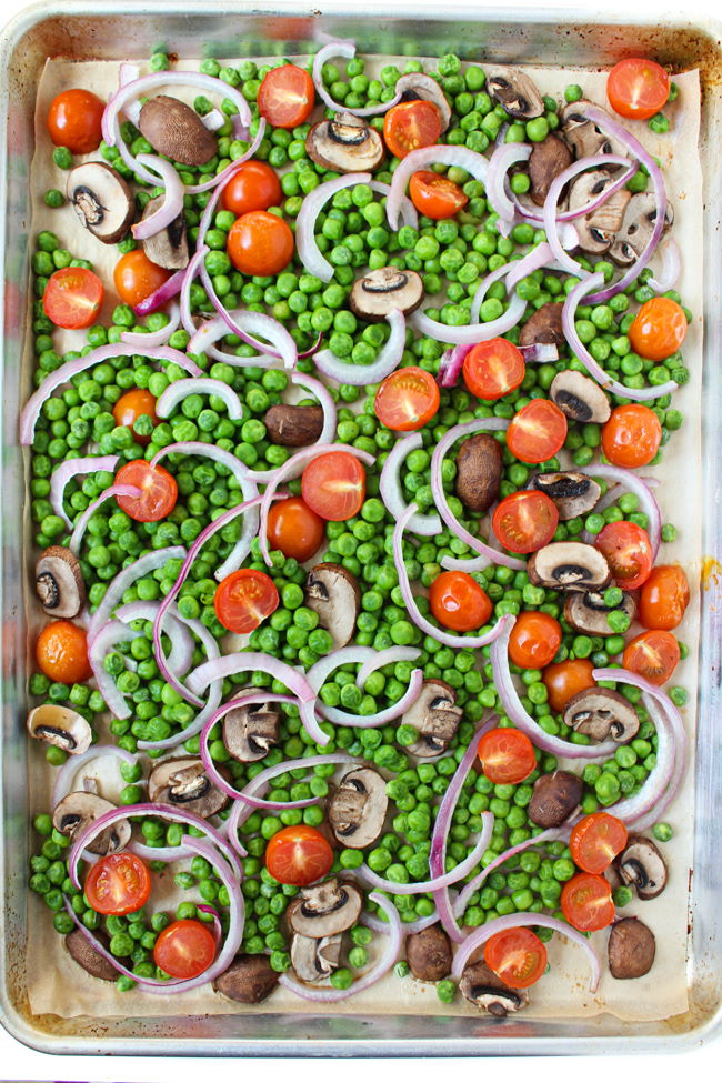 Frozen peas, mushrooms, tomatoes, and onion on a sheet pan ready to be roasted