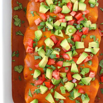 Pan of vegan bean enchiladas topped with avocado, cilantro, tomato