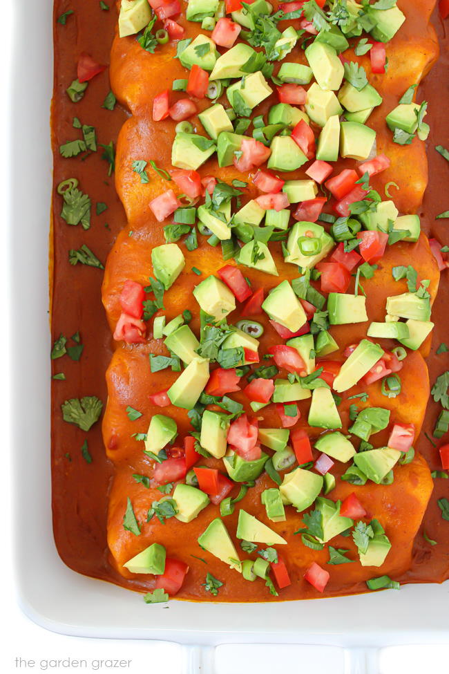 Pan of vegan bean enchiladas topped with avocado, cilantro, tomato