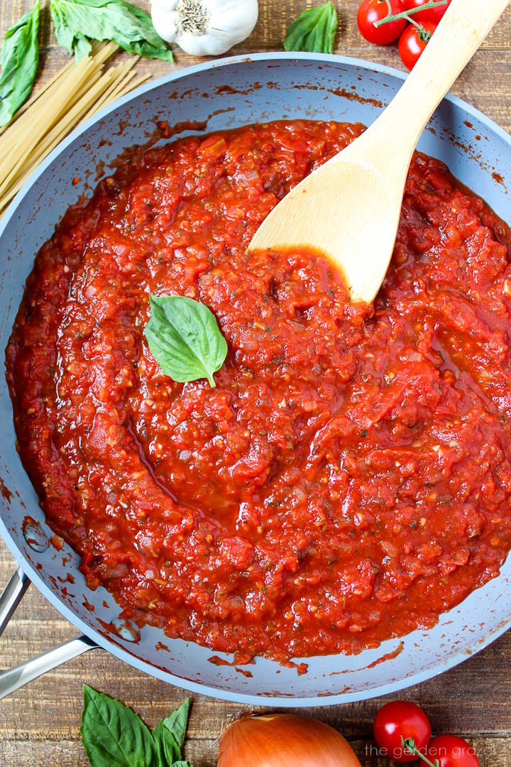 Overhead view of vegan marinara sauce cooking in a large skillet with wooden stirring spoon