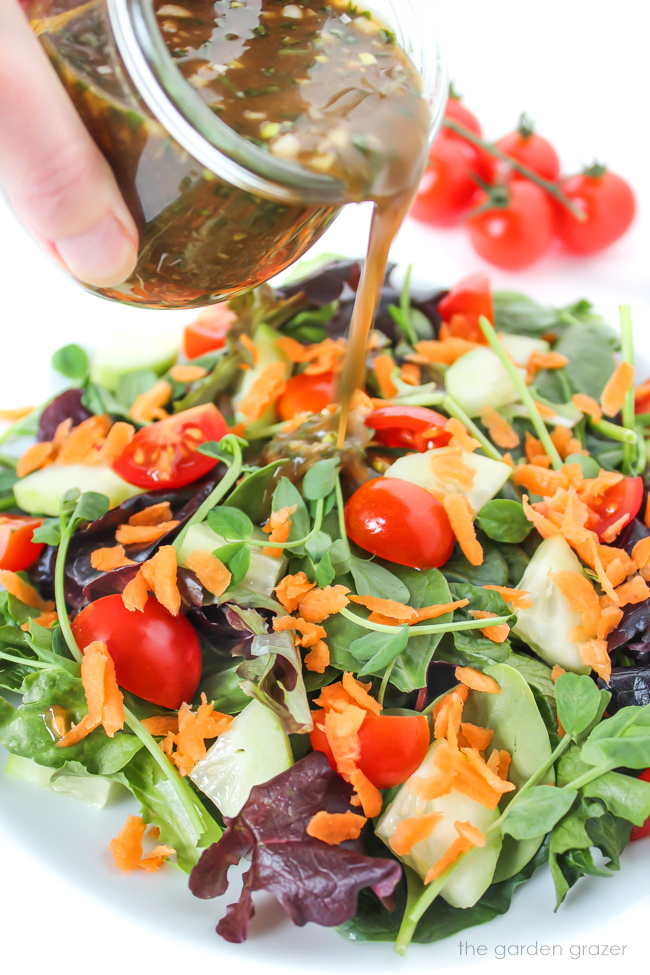 Pouring garlic balsamic dressing over a tossed salad