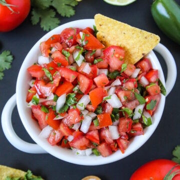 Salsa fresca in a white serving bowl with tortilla chip for dipping