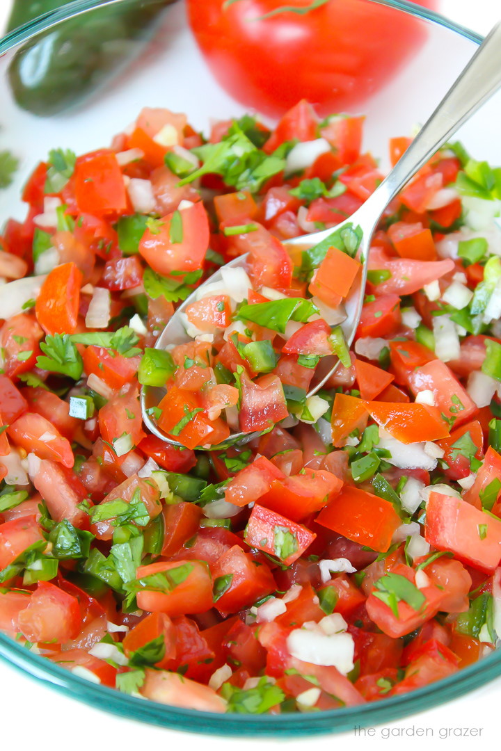 Zoomed in view of fresh salsa fresca (pico de gallo) in a glass bowl with spoon