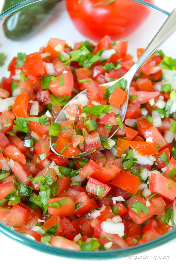 Zoomed in view of fresh salsa fresca (pico de gallo) in a glass bowl with spoon