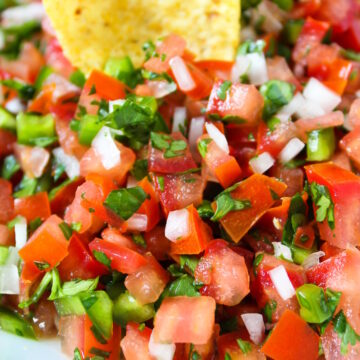 Close up view of a tortilla chip dipping into fresh salsa fresca in a serving bowl