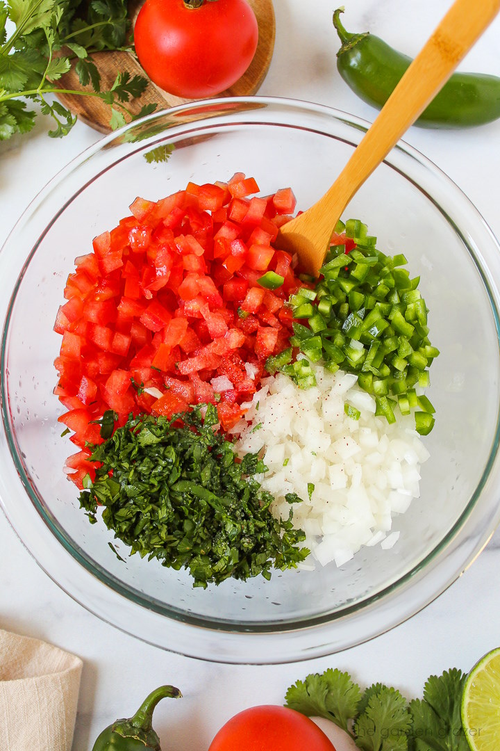 Overhead view of preparing tomato and onion ingredients in a large glass bowl before mixing together