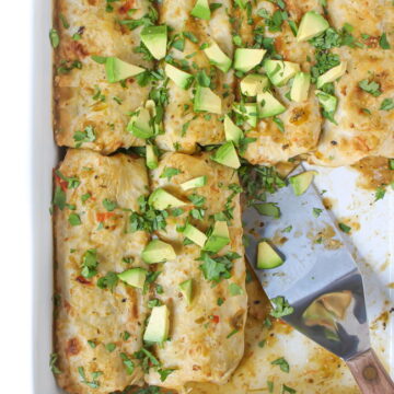 Pan of vegan green enchiladas topped with avocado and cilantro