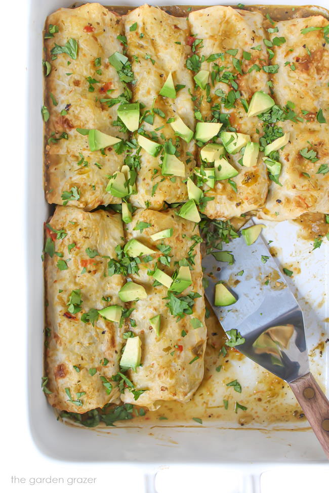 Pan of vegan green enchiladas topped with avocado and cilantro