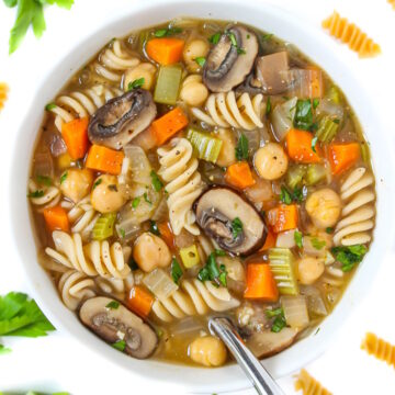 Overhead view of chickpea noodle soup in a white bowl with serving spoon