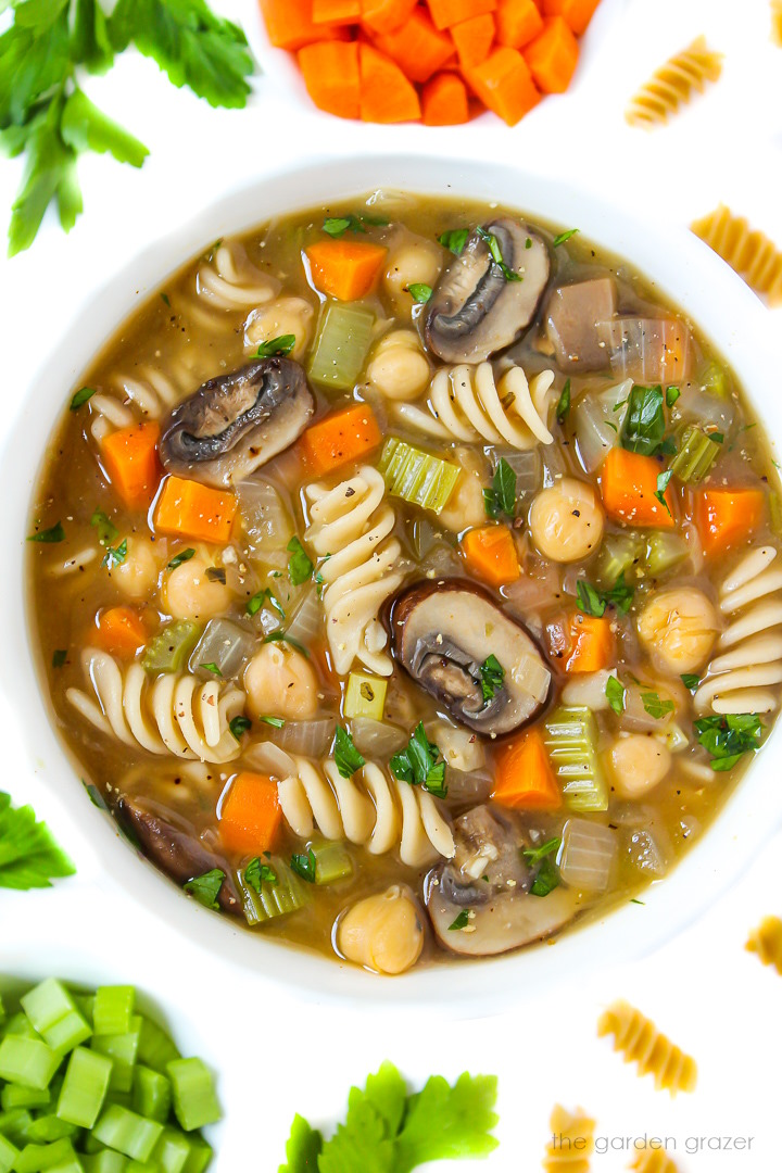 Vegan chickpea noodle soup in a white bowl with fresh parsley