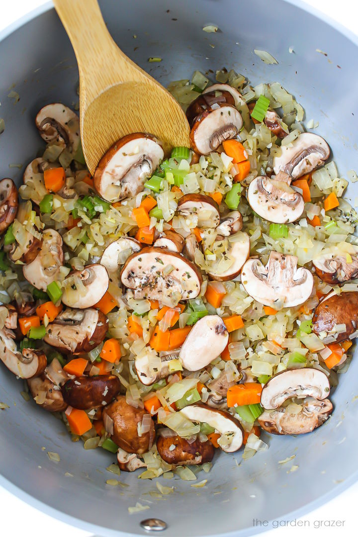 Mushrooms, onions, carrots, and celery cooking in a large stockpot with garlic and herbs