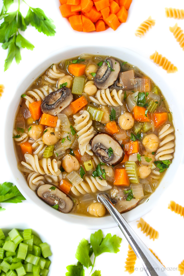 Overhead view of chickpea noodle soup in a white bowl with serving spoon