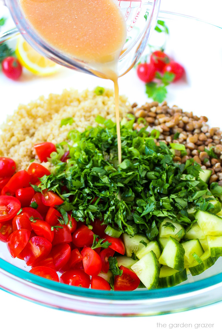 A lemon-vinegar dressing being poured over lentil quinoa salad in a large glass bowl