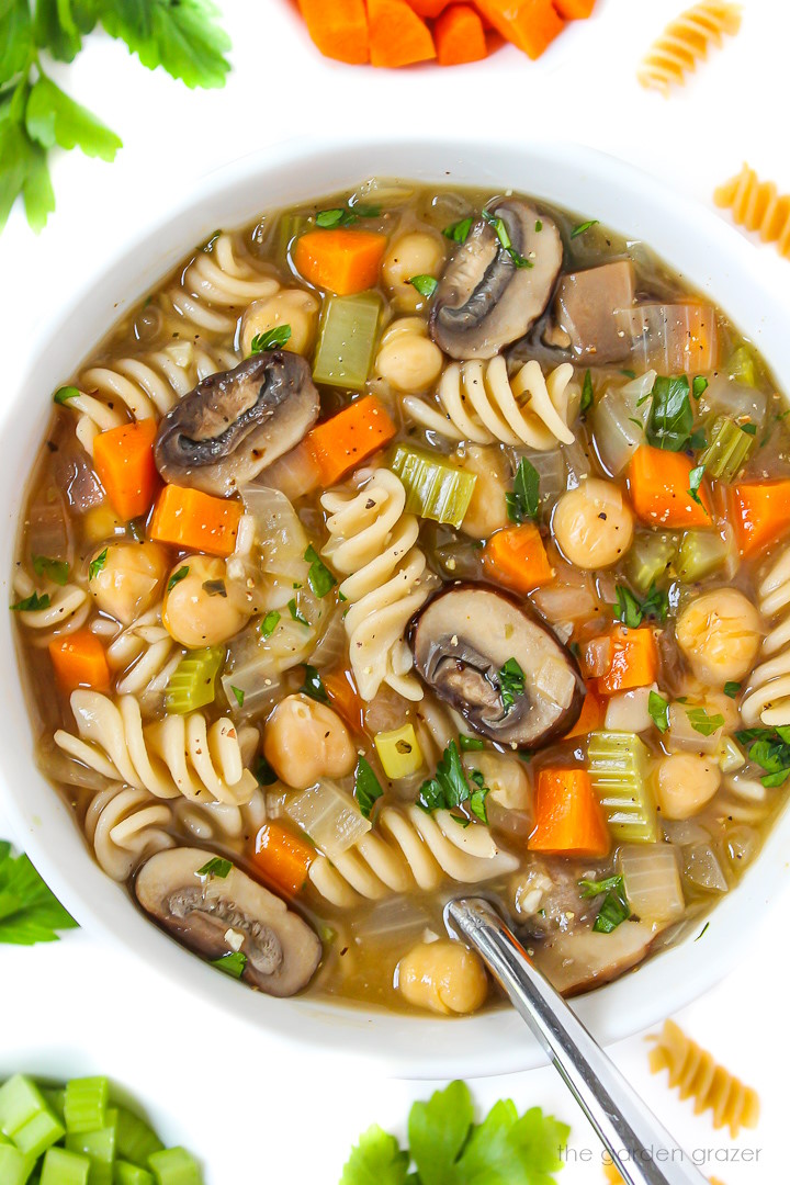 Close up view of vegan chicken noodle soup in a white bowl with spoon