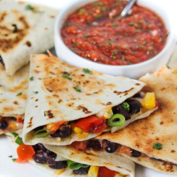 Vegan black bean corn quesadilla on a white plate with bowl of salsa