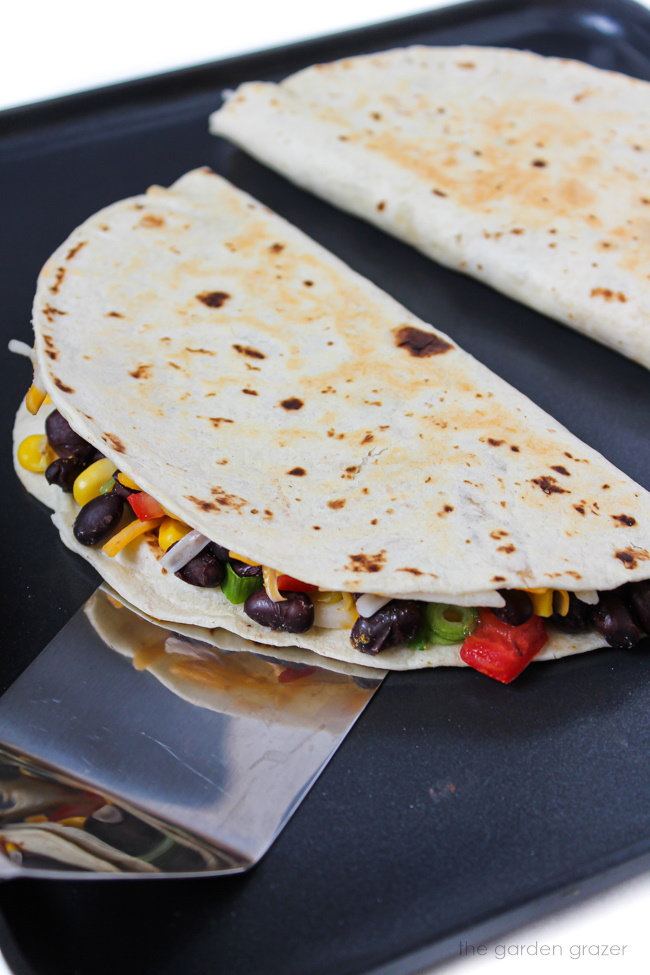 Two black bean quesadillas cooking on a skillet with spatula