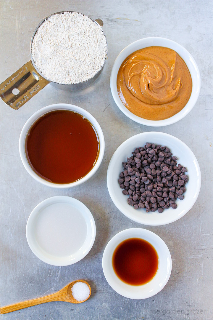 Peanut butter, oat flour, maple syrup, chocolate chips, milk, vanilla, and seasoning ingredients laid out on a metal tray