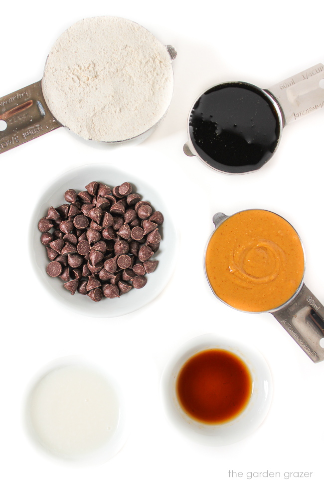 Peanut butter, chocolate chips, oat flour, milk, and vanilla extract ingredients on a white table