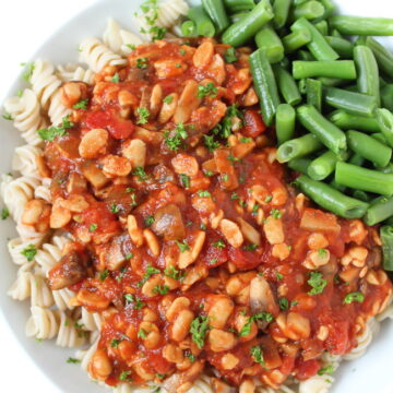 Vegan tempeh pasta on a white plate with green beans