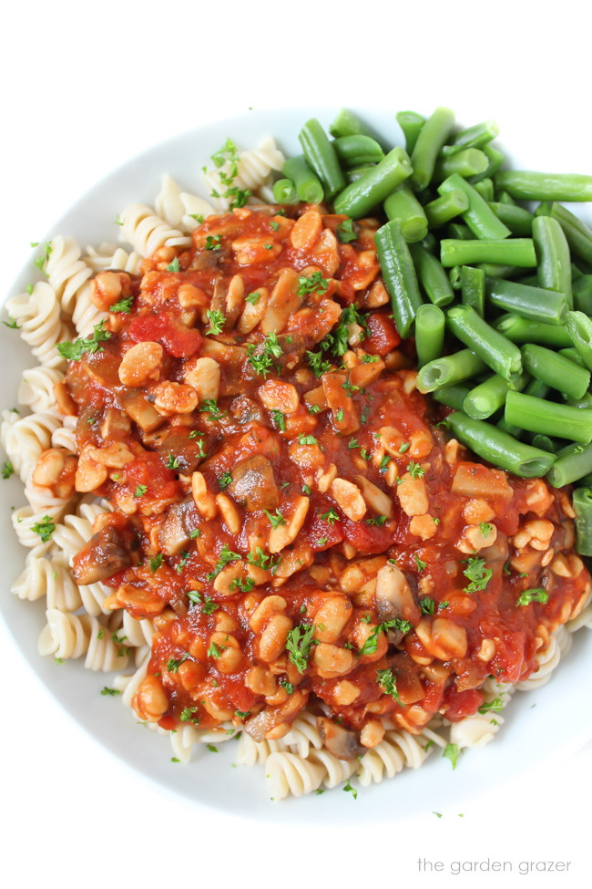 Vegan tempeh pasta on a white plate with green beans